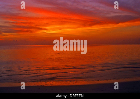 Il post-incandescenza di un tramonto tropicale è riflessa nelle nuvole sopra, che a sua volta si riflettono nel mare calmo di seguito. Foto Stock