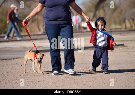 Una donna e suo figlio di due anni a piedi il loro cane in un parco. Foto Stock