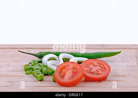 Un trito di peperoncini verdi, pomodori a fettine e le cipolle tagliate a fette in età boarrd chopping e sfondo bianco. orizzontale Foto Stock
