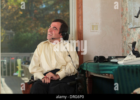 Uomo con paralisi cerebrale in sedia a rotelle motorizzata utilizzando le sue cuffie Foto Stock