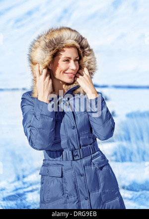 Ritratto di donna carina indossando giacca calda con cappuccio con pelliccia, divertendosi in winter park, inverno stile alla moda Foto Stock