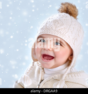 Closeup ritratto di incantevole piccola bambina indossa caldo Elegante cappello isolato blu su sfondo innevato, la caduta della neve Foto Stock