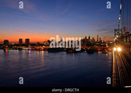 Lo Skyline di Philadelphia al tramonto dalla Ben Franklin bridge spanning Fiume Delaware in primo piano. Foto Stock