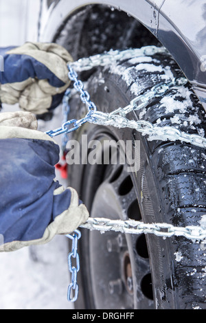 Auto conducente monta le catene da neve sul pneumatico della sua vettura Foto Stock