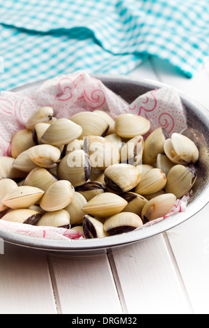 Materie le vongole nel recipiente metallico bianco sul tavolo di legno Foto Stock