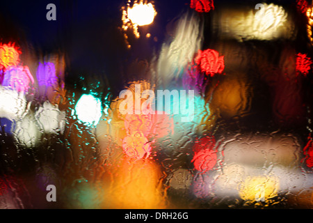 Presa luci attraverso le gocce di pioggia sul vetro di notte Foto Stock