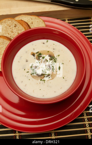 Crema di zuppa di funghi in una ciotola di colore rosso su una targhetta rossa guarnita con funghi tagliati a fettine Foto Stock