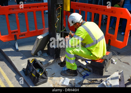 Vista posteriore ravvicinata l'ingegnere elettricista lavora sul cablaggio e sui cavi elettrici sulla colonna di illuminazione stradale di base abbigliamento ad alta visibilità Londra Inghilterra Regno Unito Foto Stock