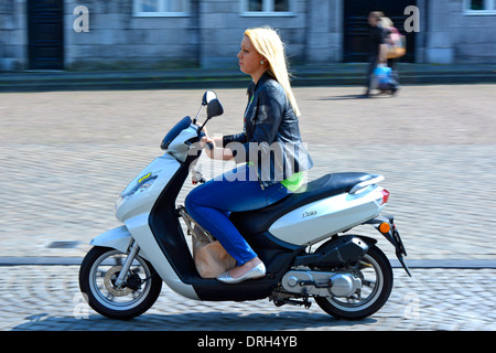 Maastricht City Side View giovane donna lunga bionda equitazione scooter borsa tra i piedi caldo luglio soleggiato Limburgo, Paesi Bassi Europa UE Foto Stock