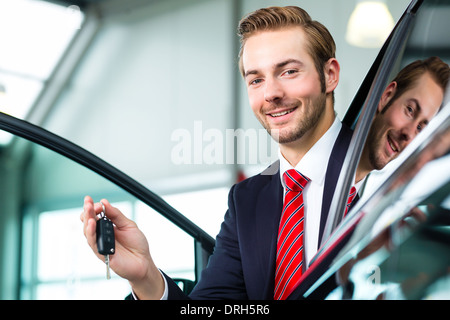 Venditore o venditore auto in concessionaria auto con chiave per presentare la sua auto nuove e usate nella showroom Foto Stock