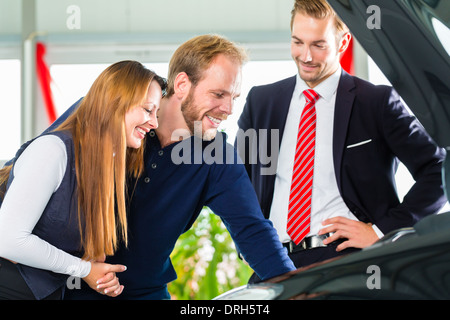 Venditore o venditore auto e i clienti o i clienti in concessionaria auto presentando le prestazioni del motore di autoveicoli nuovi e usati Foto Stock