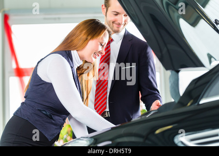 Venditore o venditore auto e client femmina o il cliente in concessionaria auto presentando le prestazioni del motore di autoveicoli nuovi e usati Foto Stock