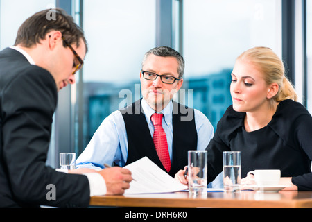 Business - giovane in un colloquio di lavoro, firma il suo contratto di lavoro con un boss e il suo assistente femmina nel loro ufficio Foto Stock