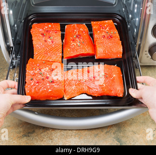 Foto di mani femminili immissione pezzi freschi di Wild rosso Salmone in forno rack con contatore di pietra in alto al di sotto Foto Stock