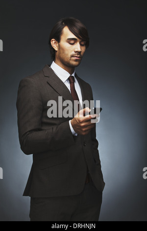 Bel giovane imprenditore la lettura di un messaggio di testo sul suo smart phone. Razza mista maschio modello di business suit utilizzando il telefono cellulare. Foto Stock