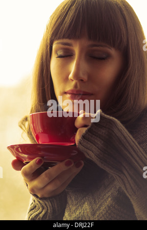 Giovane bella donna di bere il caffè o tè con vapore. Calda tonalità di colore Foto Stock