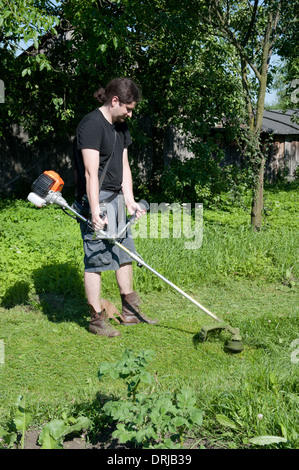 Uomo con un brushcutter lavorando in un giardino Foto Stock