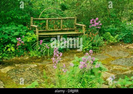 In legno realizzati a mano da banco bastoni siede in ombra giardino tra columbine, Dames rucola e felci Foto Stock