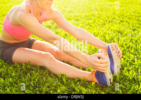 Montare attraente giovane donna stretching prima di esercizio di allenamento, sunrise la mattina presto retroilluminato con profondità di campo Foto Stock