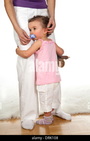 Triste bambina tenendo la sua madre per le gambe Foto Stock