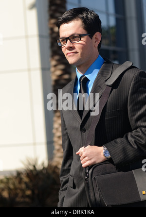 Giovane imprenditore indossando occhiali vestito in business suit holding per la cinghia della sua borsa guardando lontano Foto Stock