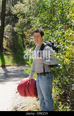 Giovane uomo andando escursioni, campeggio, essendo all'aperto in natura. Egli ha uno zaino e rosso sacco a pelo Foto Stock