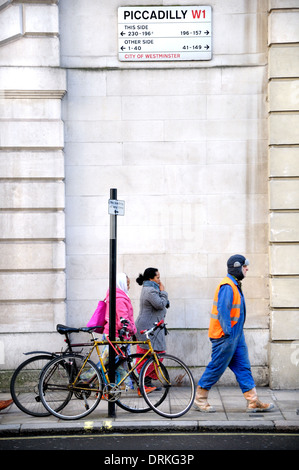 Londra, Inghilterra, Regno Unito. Piccadilly - strada segno, biciclette e persone a piedi passato Foto Stock