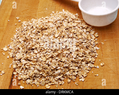 Una pila di fiocchi d'avena cruda si siede su un banco di legno alto. Foto Stock