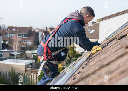 L'uomo rendendo la costruzione di pannelli solari ad alta sul tetto Foto Stock