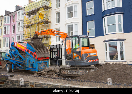 Dopo una settimana di alta marea, mareggiate e tempesta vigore venti, il lungomare di Aberystwyth in Galles è stato devastato, con milioni di £ 's di danni. Le onde che si infrangono punzonato un grande foro nella parete del mare ed è crollato Aberystwyth iconici, lungomare vittoriano rifugio, che ha resistito per oltre 100 anni. Questa foto è stata scattata mercoledì 8 gennaio, 2014, il giorno in cui il Consiglio ha cominciato a cercare di cancellare le migliaia di tonnellate di macerie spiaggia fuori di fronte al mare su strada. Foto Stock