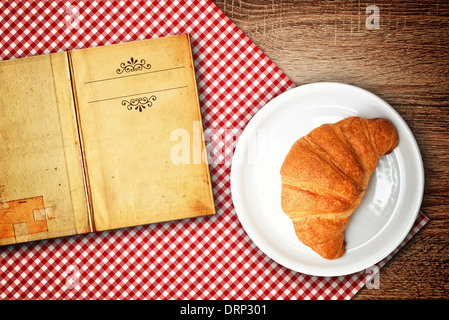 Croissant ricetta. Croissant su una piastra e vecchi aprire ricettario con copia spazio per il tuo testo. Foto Stock