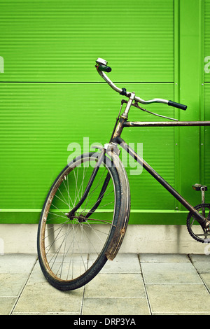 Vecchia bicicletta appoggiata sulla parete verde il vecchio incontra il nuovo concetto. Foto Stock