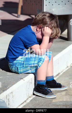 Piccolo Ragazzo seduto sui gradini con testa in mani