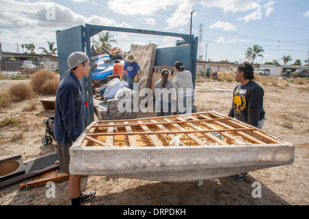 Un team di asiatici e americani di origine ispanica teens rimuovere il cestino da un deturpato vacante lot in una baraccopoli di Stanton, California. Nota cassonetto in background. Foto Stock