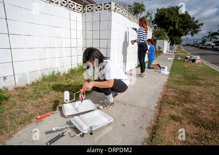 Un volontario del team americano asiatico ragazze teenager viene aggiornata in pareti esterne in una delle baraccopoli di Stanton, California, come parte di una campagna di pulizia. Foto Stock