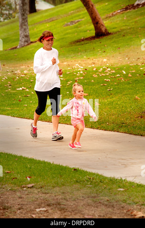 Una bambina corre attraverso un parco in Costa Mesa, CA, come sua nonna segue il suo. Foto Stock