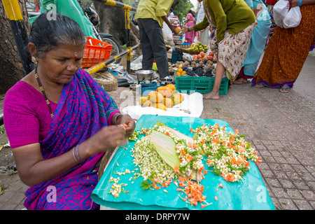 Una donna che fa floral decorazioni capelli ad una strada del mercato di Mysore, India. Foto Stock