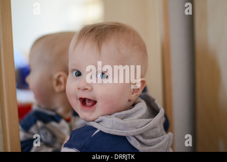 Ritratto di otto mesi baby boy davanti a uno specchio cercando curioso alla fotocamera Foto Stock