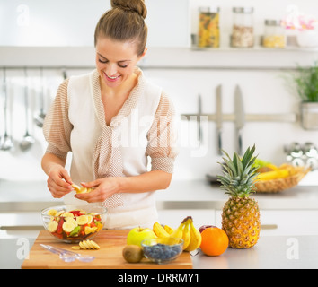 Giovani casalinga rendendo insalata di frutta in cucina Foto Stock