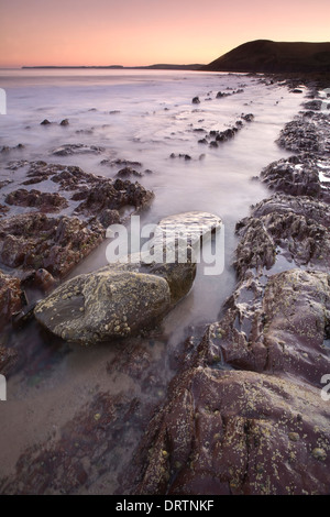 Rocce frastagliate essendo coperto dalla marea al tramonto di Manorbier Beach, Pembrokeshire, South Wales, Regno Unito Foto Stock