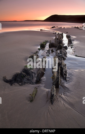 Rocce frastagliate che sporgono dalla sabbia a bassa marea durante il tramonto su Manorbier Beach, Pembrokeshire, South Wales, Regno Unito Foto Stock