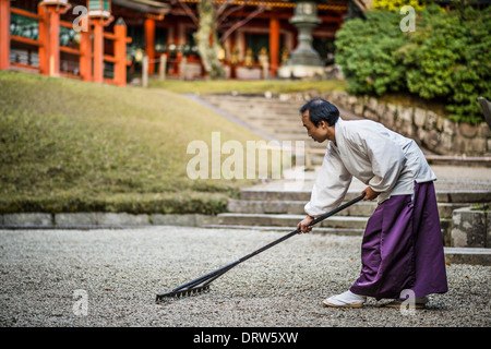 Lo Shintoismo giapponese sacerdote rastrelli un giardino di roccia. Foto Stock
