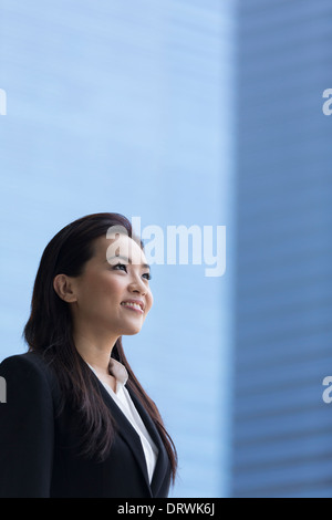 Chinese business donna nella moderna città asiatiche. Asian imprenditrice sorridente e guardando la telecamera con sfocato edifici per uffici a Foto Stock