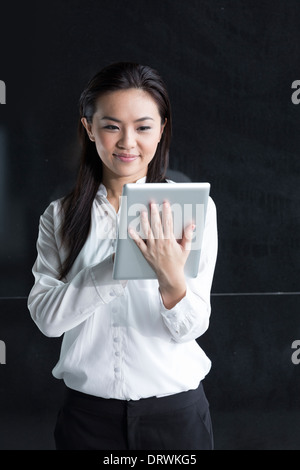 Donna cinese con un computer tablet. Asian business donna tramite digital computer tavoletta appoggiata contro una parete nera. Foto Stock