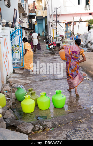 Le donne indiane il riempimento di bicchieri in plastica con acqua da un tubo montante in un territorio rurale villaggio indiano street. Andhra Pradesh, India Foto Stock