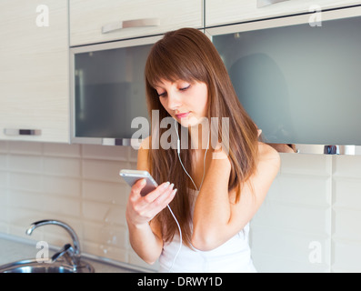 Giovane donna in cucina ascoltando musica sulle cuffie Foto Stock