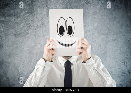 Imprenditore tenendo la carta con faccina sorridente davanti alla sua testa. Happy businessman, ufficio situazione. Foto Stock