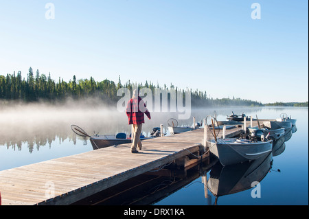 Fisherman camminando lungo il molo al mattino presto il lago di nebbia. Foto Stock