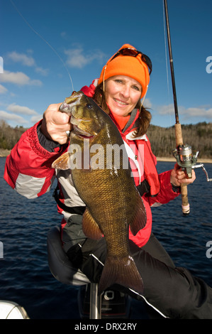 Donna pescatore tenendo in mano un'enorme smallmouth bass catturato da una barca sul lago Ontario del nord. Foto Stock