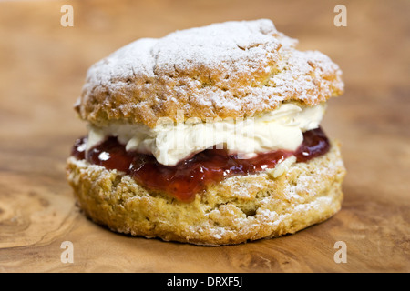 Scone riempita con marmellata e crema fresca su una tavola di legno. Foto Stock